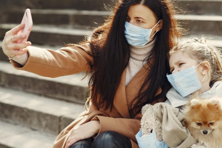 A mother and daughter wearing masks take a selfie outdoors during COVID-19 with their pet dog.