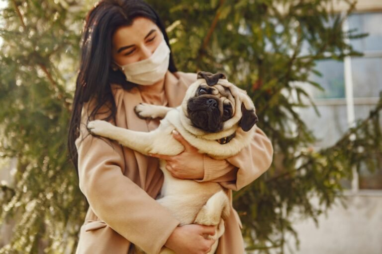 Woman with mask holding a cute pug outside by trees. Capturing a heartwarming moment.